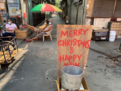 Vendors wearing face masks amid concerns of the Covid-19 coronavirus sit near a sign and a basin for alms hours before Christmas eve in Manila on December 24, 2020. (Photo by TED ALJIBE / AFP)