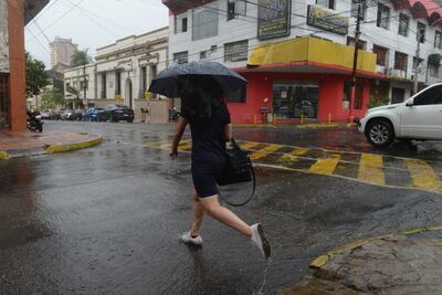Un hombre se protege de la lluvia con un paraguas mientras cruza una calle en el microcentro de Asunción.