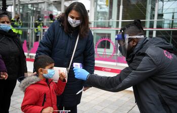 Un trabajador toma la temperatura de los clientes mientras hacen cola para abordar una cápsula en la atracción turística reabierta del London Eye, en Londres.