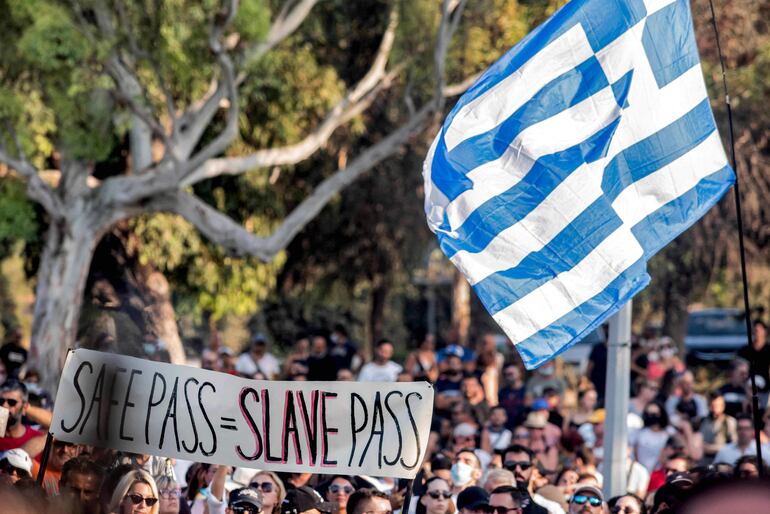 Demonstrators raise a Greek flag as people gather outside the presidential palace in Cyprus' capital Nicosia on July 18, 2021, in protest against new COVID-19 coronavirus pandemic safety measures introduced by the government amidst a recent rise in infection figures. - Cyprus is suffering a fourth wave of coronavirus driven by the aggressive Delta variant, with infections the prior week hitting four digit figures. (Photo by Iakovos Hatzistavrou / AFP)