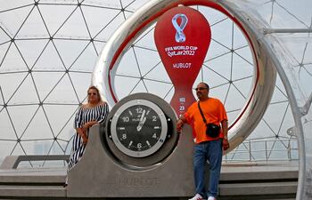 Dos turistas posan en Doha junto al reloj que marca la cuenta regresiva para el Mundial de Qatar, cuyo inicio podría adelantarse un día, para el 20 de noviembre.