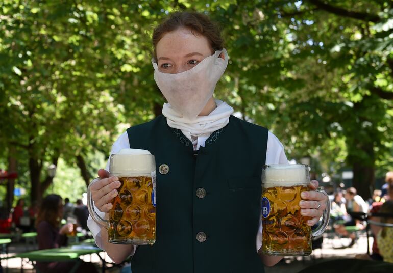 Una camarera con mascarilla lleva dos vasos de cerveza en Munich, Alemania.