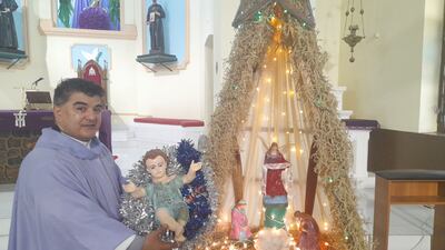El cura párroco José Villalba, con el niño Jesús en mano al lado del pesebre de la Catedral de Fuerte Olimpo.