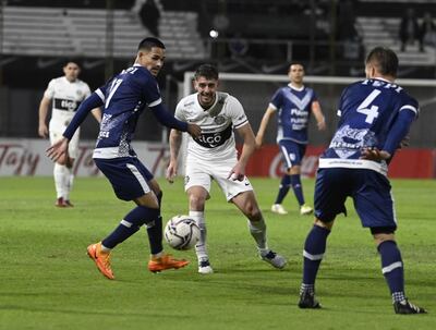 Alejandro Silva intenta un pase para un compañero ante la marca de dos jugadores de Ameliano