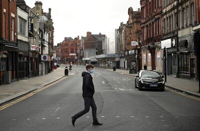 Un hombre con tapabocas cruza una carretera casi vacía en el centro de Bolton, en el norte de Inglaterra.