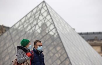 Peatones con mascarillas de protección caminan junto a la pirámide del Louvre, en París.