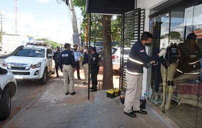 Agentes policiales de Criminalística toman huellas dactilares de la puerta de vidrio de la boutique.