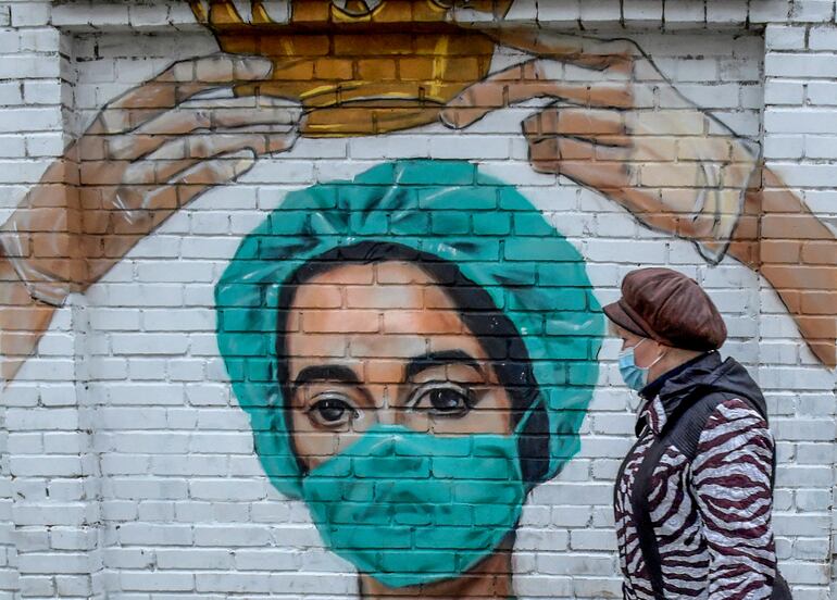 Una mujer con mascarilla camina junto a un mural que muestra a una trabajadora de la salud en San Petersburgo, Rusia.