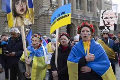 Manifestantes con banderas ucranianas cantan el himno nacional ucraniano durante una manifestación contra la invasión rusa frente al edificio del parlamento suizo en Berna, Suiza, el 19 de marzo de 2022.