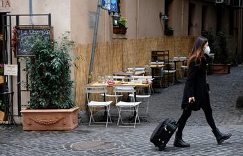 A woman wearing protective mask pulls a trolley bag as she walks past empty cafe tables as the government brings in new restriction measures to curb the spread of COVID-19 novel coronavirus, in central Rome on November 5, 2020. (Photo by ANDREAS SOLARO / AFP)
