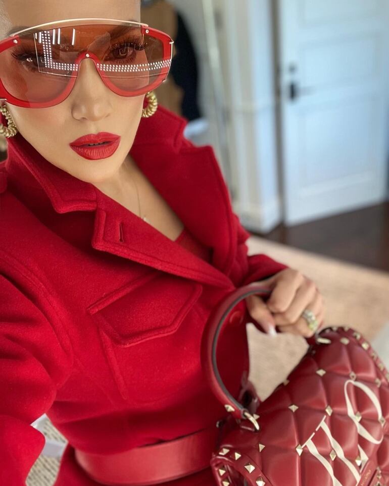 El traje rojo de J Lo fue complementado con accesorios en el mismo tono, donde se destacaron la cartera con sus iniciales y unos mega anteojos. (Instagram/Jennifer López)