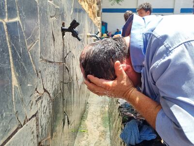Un hombre se refresca la cabeza con agua de la canilla, como una forma de aplacar el intenso calor.