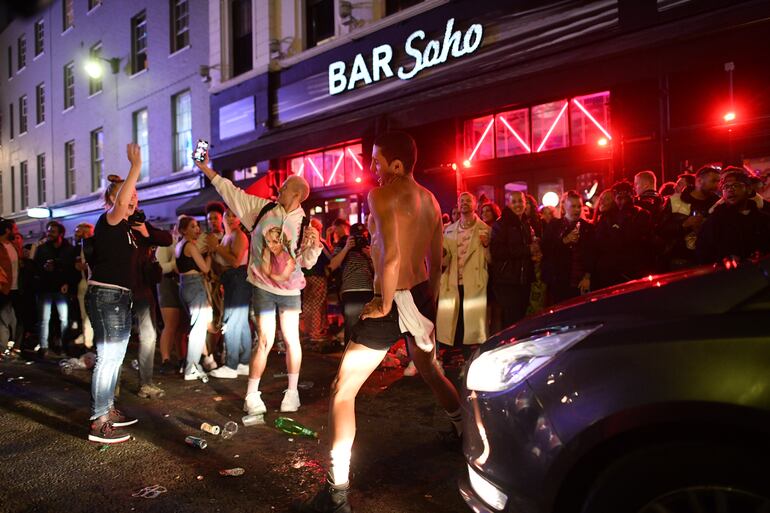Un auto intenta cruzar una calle llena de personas que acudieron a la reapertura de los pubs en la zona de Soho, en Londres, el pasado sábado.