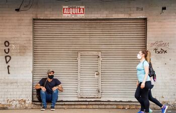 Dos personas con tapabocas caminan por una calle del microcentro asunceno, frente a un negocio en alquiler.