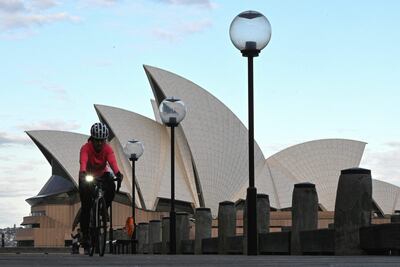 Una mujer pedalea su bicicleta frente a la Ópera de Sídney, en Australia, durante el confinamiento.