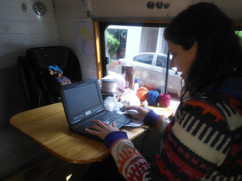 Jessica Serra, trabajando en su notebook. Al lado se observan los hilos de colores con los que elaboran pulseras, collares, entre otras obras de artesanía destinadas a la venta para cubrir los gastos del viaje.