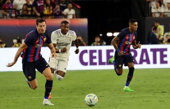 Robert Lewandowski (i) y Raphinha (d), del Barcelona, corren en procura del balón ante la presencia de David Alaba, del Real Madrid.