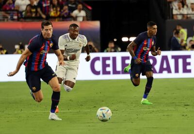 Robert Lewandowski (i) y Raphinha (d), del Barcelona, corren en procura del balón ante la presencia de David Alaba, del Real Madrid.