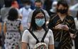 En primer plano, una mujer con mascarilla camina entre una multitud en Kuala Lumpur.