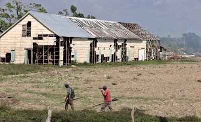 Cubanos caminan cerca de una casa de secado de las hojas del tabaco afectada por el paso del huracán Ian, en San Juan y Martínez, en la provincia de Pinar del Rio (Cuba).