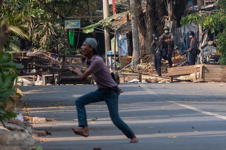 A protester runs as a security force (top L) aims a gun during a demonstration against the military coup in Mandalay on March 2, 2021. (Photo by STR / AFP)
