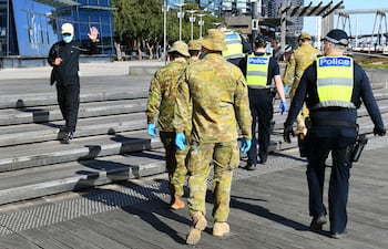 Un hombre saluda a un grupo de policías y soldados que patrullan el área de Docklands en Melbourne el 2 de agosto de 2020, después del anuncio de nuevas restricciones para frenar la propagación del coronavirus COVID-19.