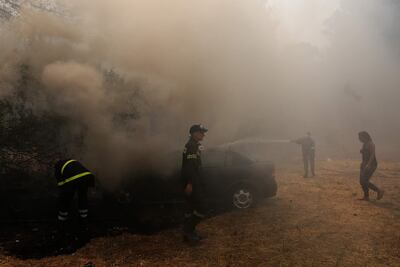 Los bomberos arrojan agua sobre un automóvil en llamas durante un incendio forestal en el área de Varybobi, al noreste de Atenas, Grecia.