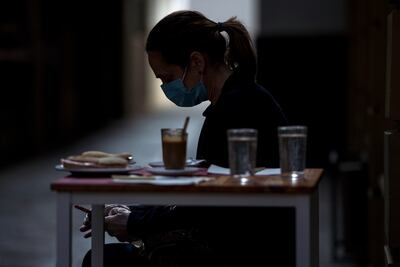 Una mujer con tapabocas revisa su teléfono antes de desayunar en una cafetería en Sevilla.