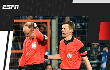 Christian Gittelmann (i), juez línea que fue agredido en la cabeza, abandona el campo junto al árbitro Benjamin Cortus.