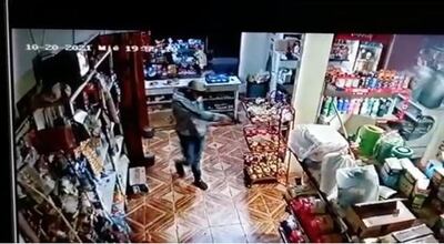 Uno de los delincuentes con pistola en mano intima al propietario de la despensa.