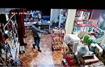 Uno de los delincuentes con pistola en mano intima al propietario de la despensa.