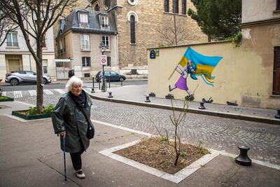 Una mujer pasa frente a un mural que representa a una niña sosteniendo una bandera ucraniana mientras pisa tanques militares, en París, Francia.