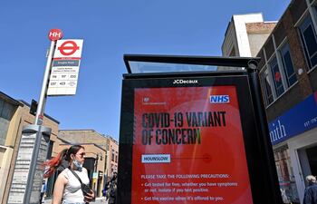 Una mujer espera en una parada de autobús junto a un letrero que advierte al público sobre una "variante preocupante del coronavirus" en Hounslow, al oeste de Londres.