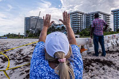 Una mujer reza con las manos dirigidas hacia los restos del sector del condominio Champlain Towers South que se derrumbó en Surfside, Florida.