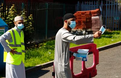 Un musulman distribuye mascarillas para entrar en la mezquita de Jamia, en Manchester.