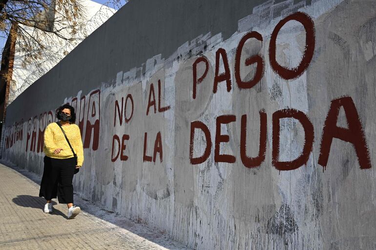 Una mujer camina junto a un muro pintado con la leyenda "No al pago de la deuda", en Argentina.