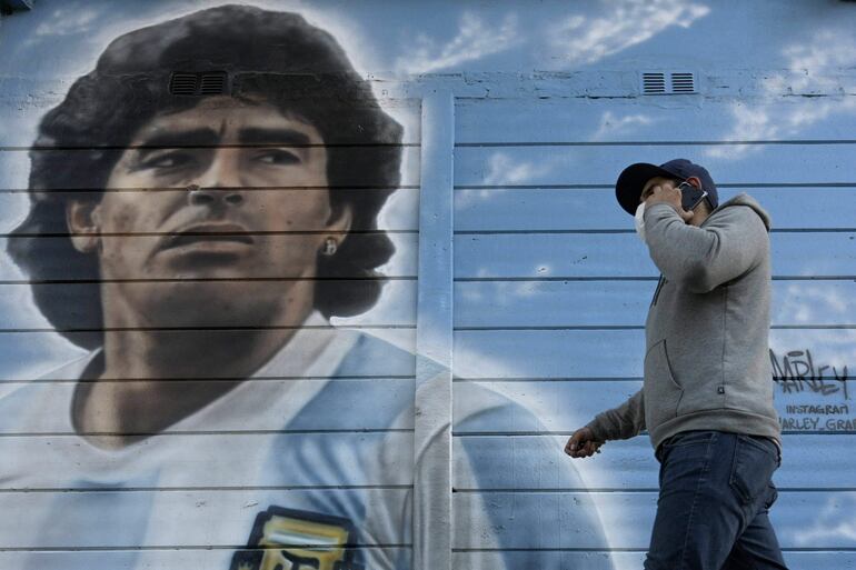 Un peatón pasa junto a un mural pintado con el retrato de Diego Armando Maradona junto al estadio que lleva su nombre en Italia.