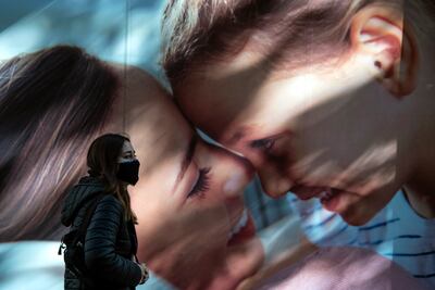 Una mujer con mascarilla camina junto a un cartel publicitario en Santiago, Chile.