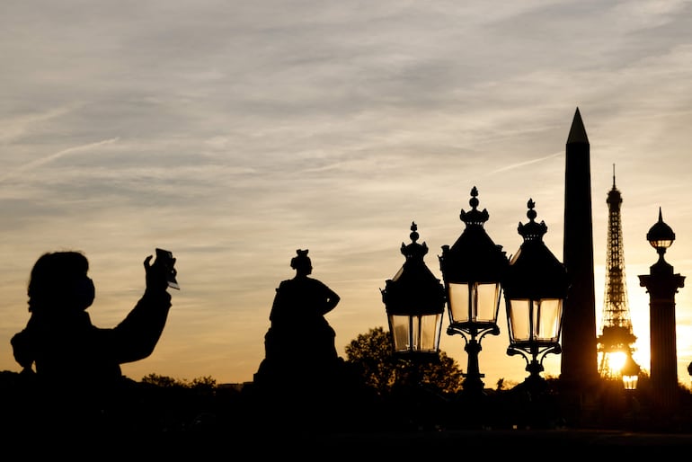 Una mujer toma una foto de recuerdo del obelisco de Luxor y la Torre  Eiffel mientras se pone el sol en París. 