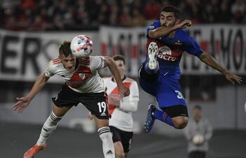 El defensor de Tigre Víctor Cabrera (d) salta con los tapones altos en procura de rechazar el balón, que intenta cabecear Braian Romero, delantero de River Plate.