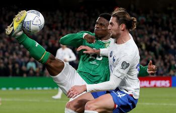El irlandés Chiedozie Ogbene puntea el balón ante el francés Adrien Rabiot.