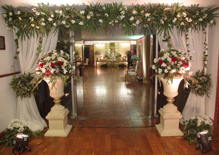 La entrada al salón ambientado con arreglos de flores y luces.

