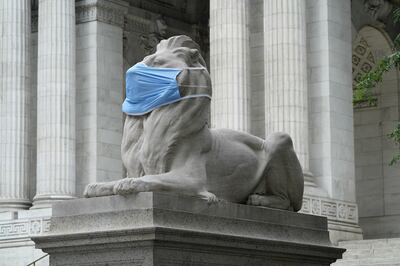 Una estatua de mármol de un león con una mascarilla puesta, frente a la Biblioteca Pública de Nueva York.