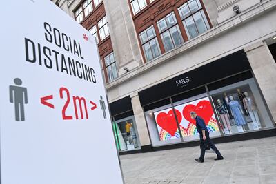 Un comprador enmascarado como medida de precaución camina frente a una tienda de Marks and Spencer en Londres. A la izquierda un cartel que indica que se debe mantener una distancia de dos metros entre las personas.