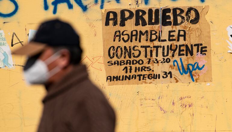 Un hombre con mascarillas pasa junto a un muro con graffiti sobre el presbícito.