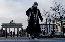 Un peatón con tapabocas camina frente a la Puerta de Brandenburgo en Berlín, Alemania.