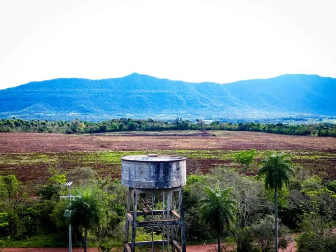 El tanque de agua ubicado en el barrio San Antonio, rodeado de la imponente Cordillera del Ybytyruzú y la parcela para cultivo posiblemente de soja.