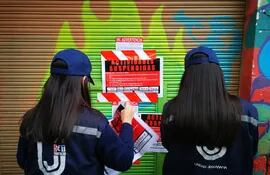 Dos funcionarias de la SET colocan carteles anunciando la suspensión de actividades en un portón del centro cultural La Chispa, en el microcentro de Asunción.