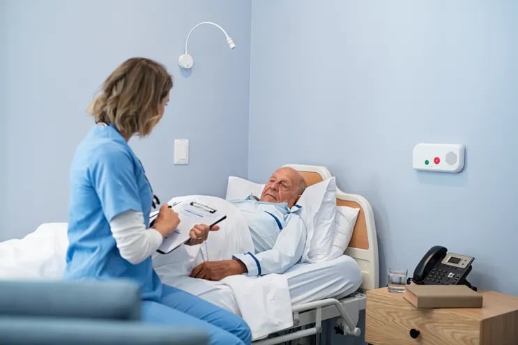 Un paciente convalece en una cama de hospital mientras recibe la visita de una enfermera