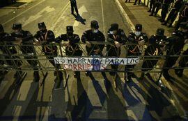 Policías resguardan vallas y se visualiza un cartel contra los corruptos en el sexto día de protestas contra el gobierno Mario Abdo, en el microcentro de Asunción, el miércoles 10 de marzo de 2021.